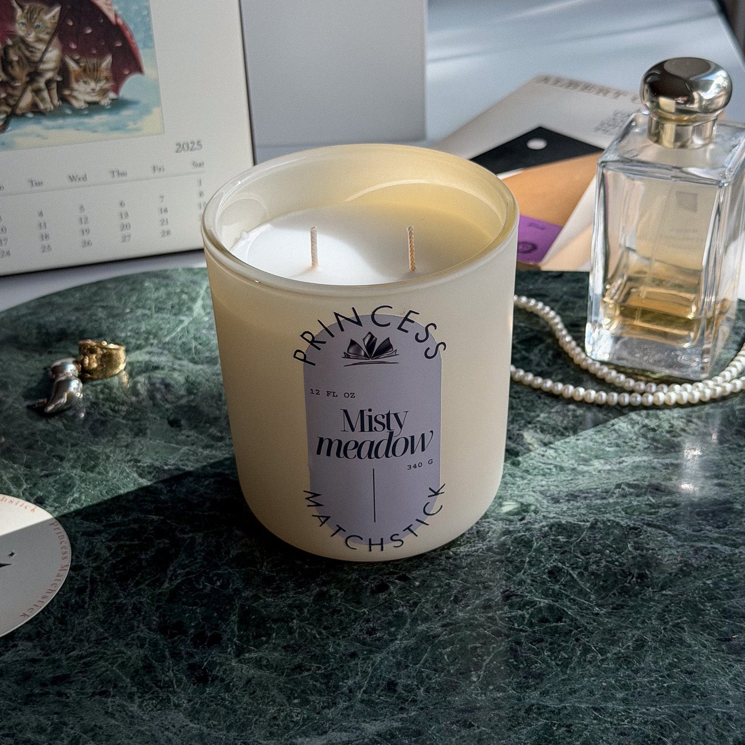 Candle labeled 'Princess' on a marble surface with a calendar and perfume bottle in the background.