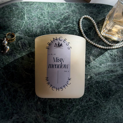 Candle labeled 'Princess' on a marble surface with jewelry and a perfume bottle.