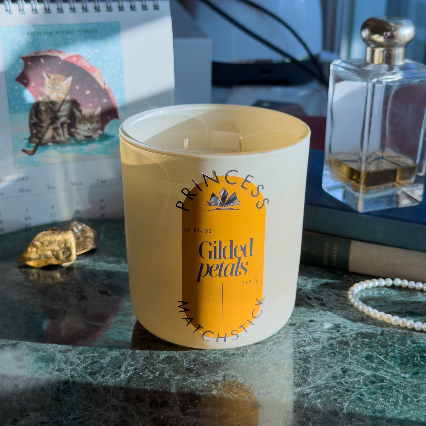 Candle labeled 'Princess' on a marble surface with a notebook and perfume bottle in the background.