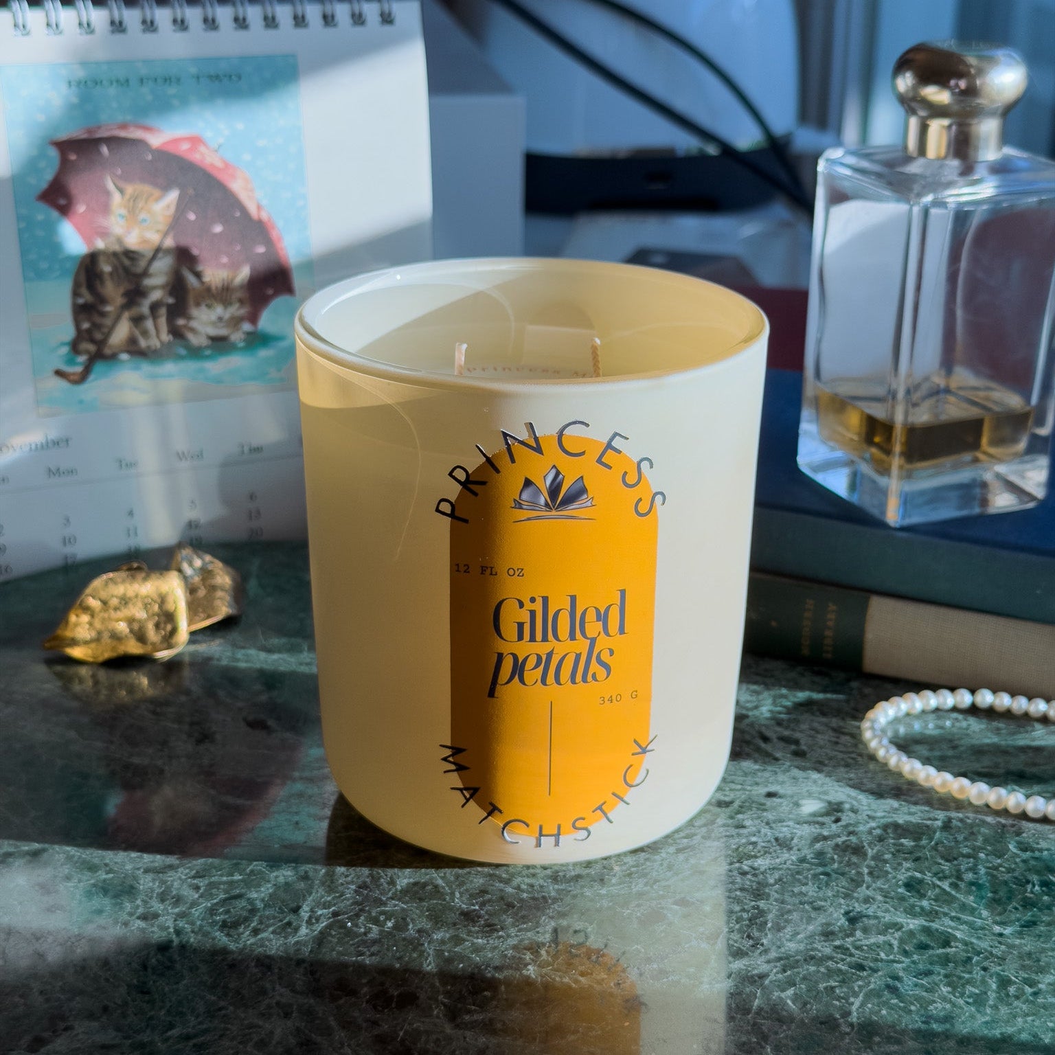 Candle labeled 'Princess' on a marble surface with a notebook and perfume bottle in the background.